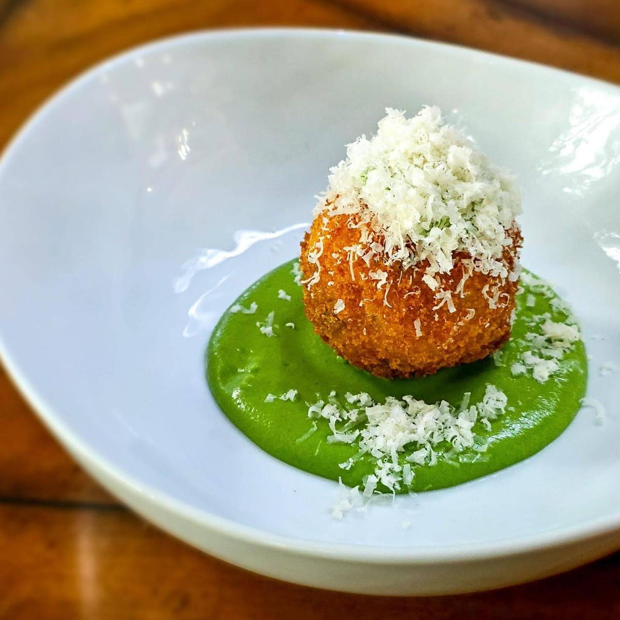 Golden arancini croquette with shaved pecorino cheese over basil velouté
